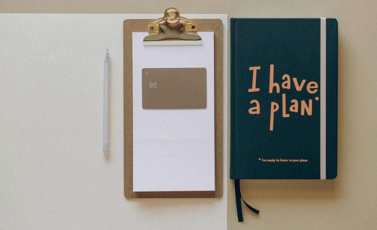 A minimalist office setup featuring a planner, clipboard, card, and pen, perfect for planning and organization.